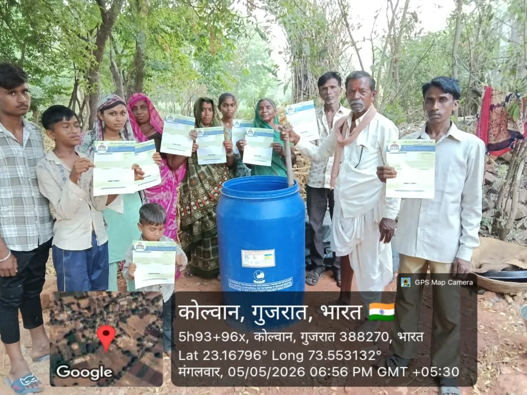Rural families holding participation documents beside a blue agricultural input drum